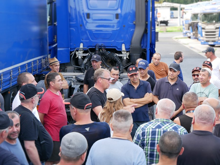 Eine Gruppe von LKW-Fahrern stehen um eine Beraterin von Faire Mobilität und einen Gewerkschafter und führen ein Gespräch.